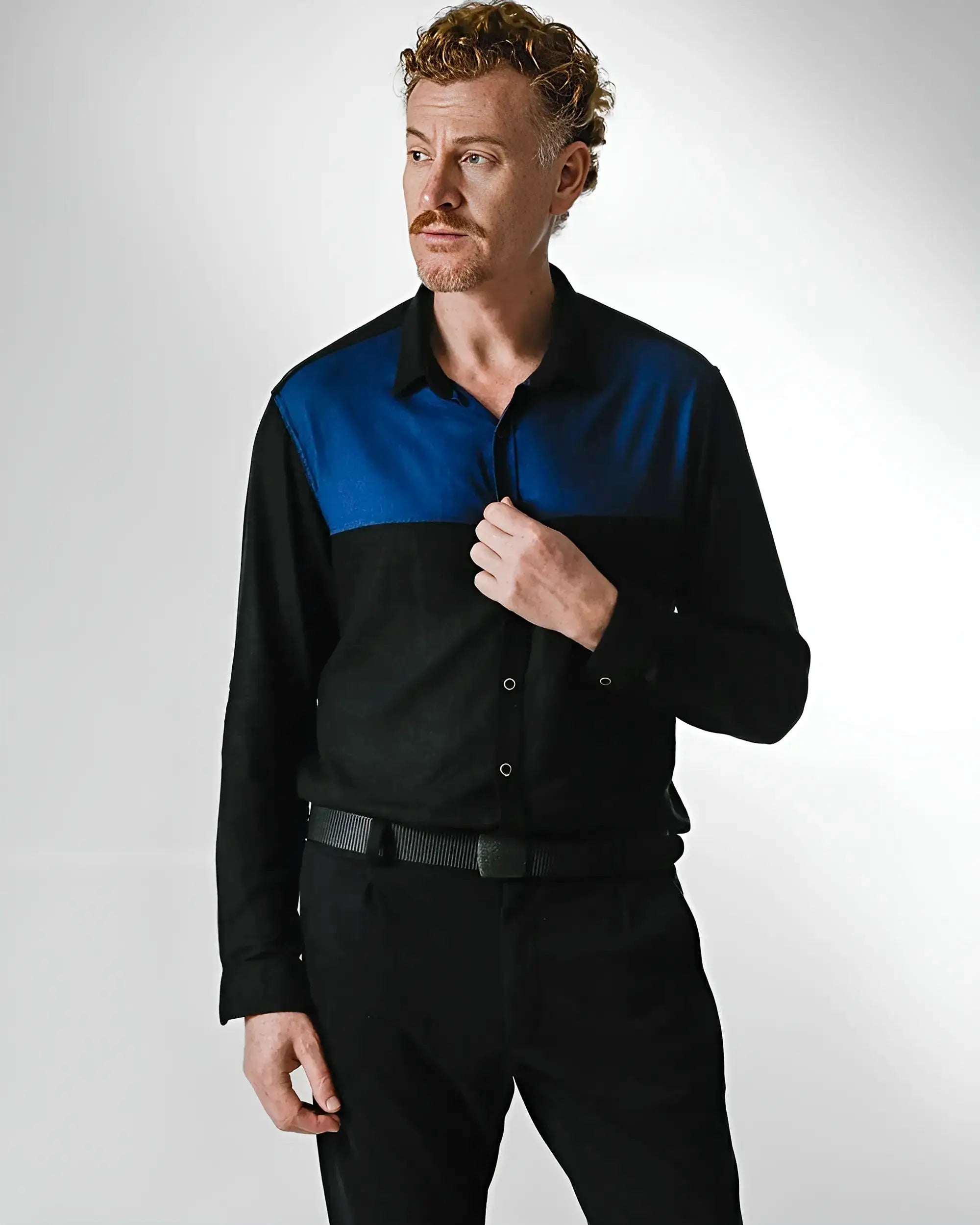 Modelo usando Camisa masculina de botão nas cores preta com recorte azul no peito.